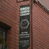 Black sign for 1:46 watch repair with white text and a watch illustration on a brick wall.